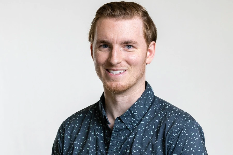 middle aged man with brown hair in grey shirt smiling against grey wall